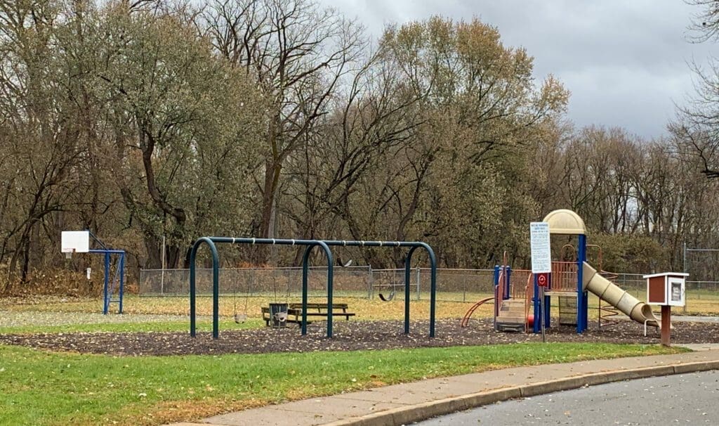 A photo of a city park with swings and a tube slide.