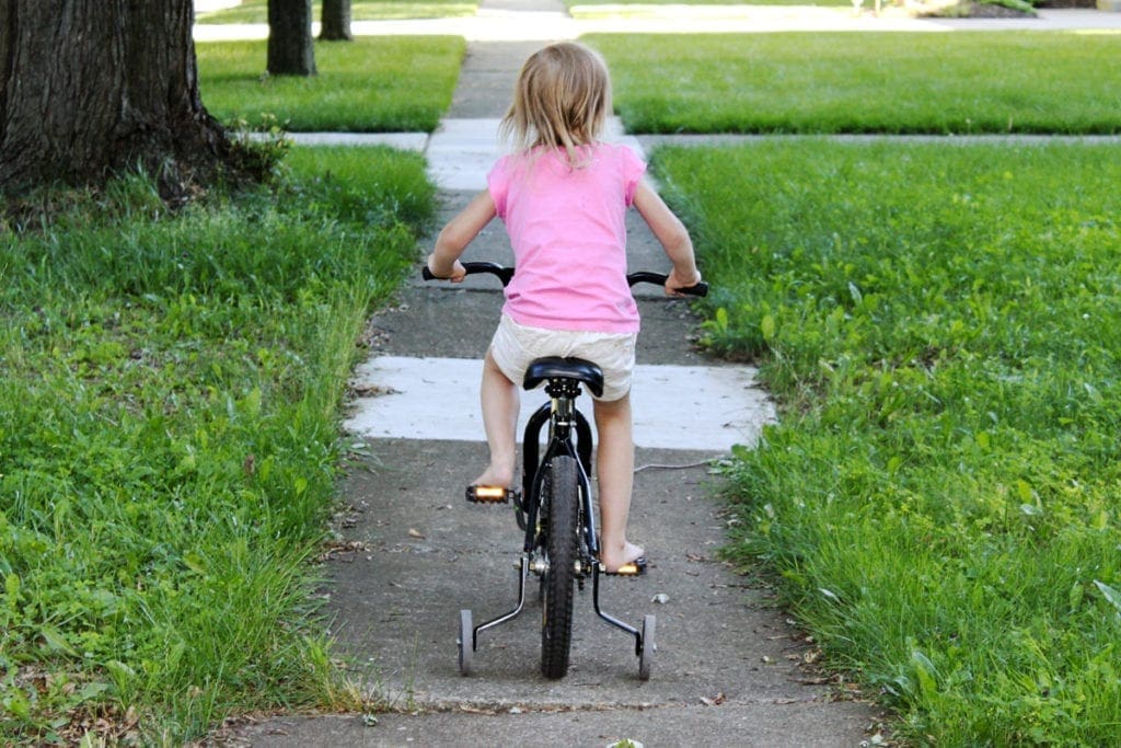 A little girl riding s bike with training wheels.