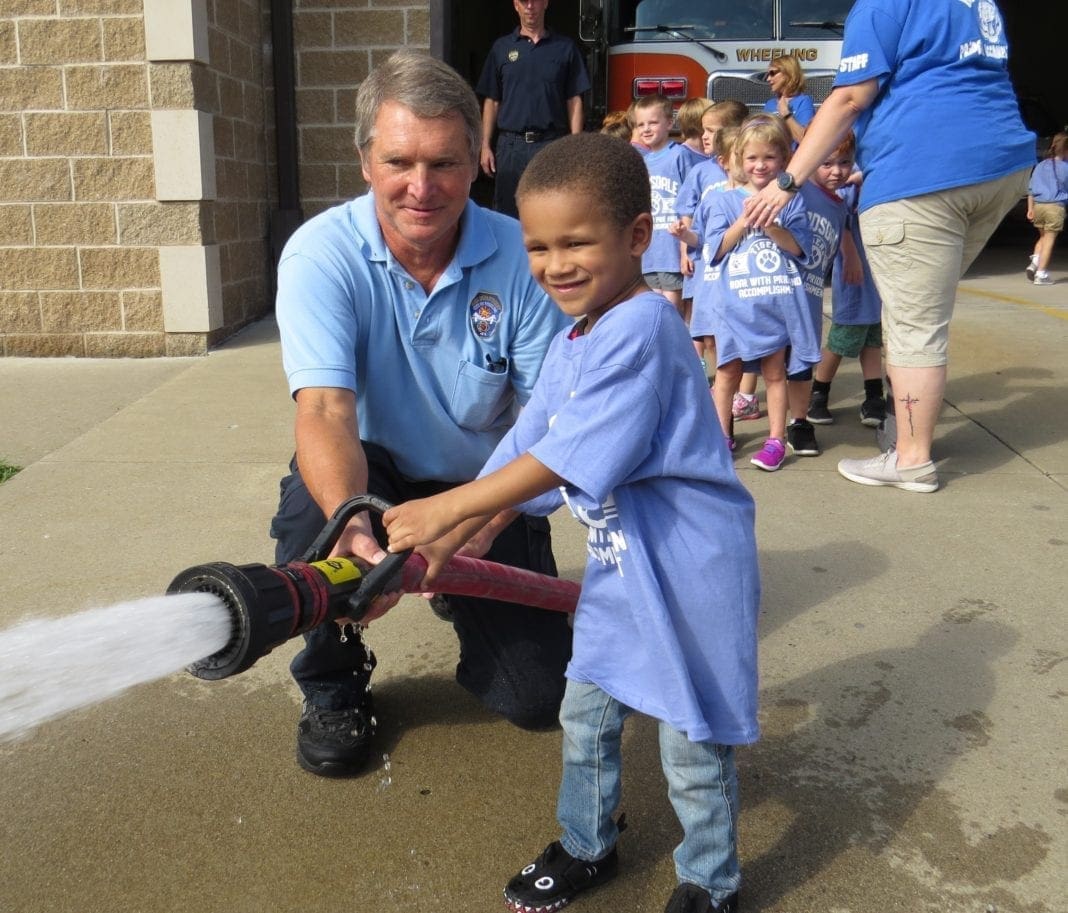 A child and a firefighter using a hose.