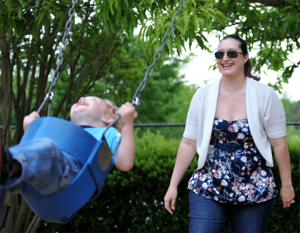 A mother swinging her child in a park swing.