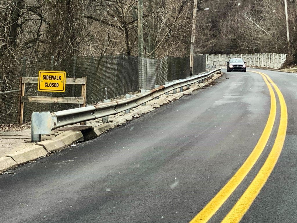 A photo of a dilapidate sidewalk near a road.