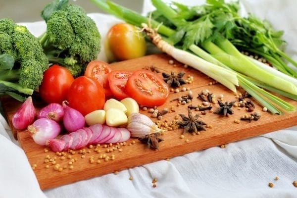 A photo of a cutting board that has onions, tomatoes, and celery on it.