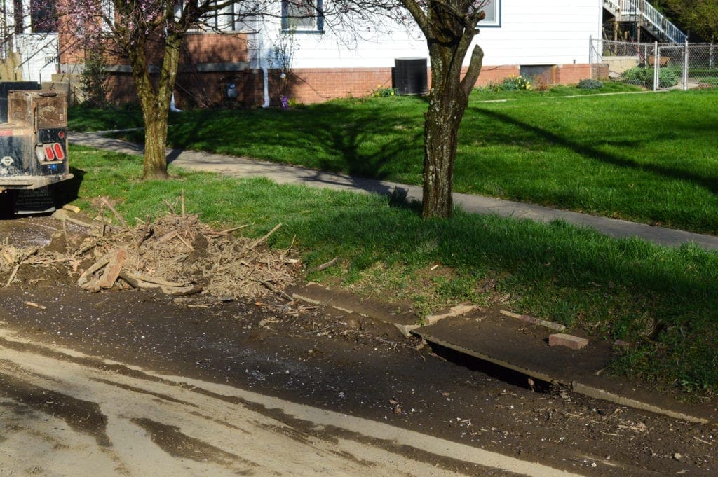 A photo of a lot of run-off debris near a sewer.