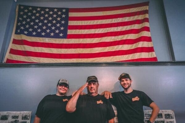 Kelly, Scott and Kyle Phair pose in front of a large American flag hung on the wall inside Country Roads BBQ