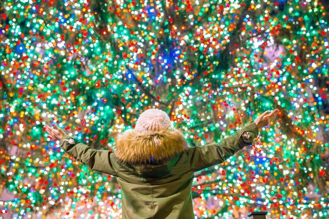 A child in front of a tree full of lights.