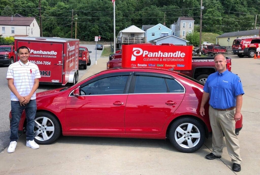 A photo of two men with a red car.