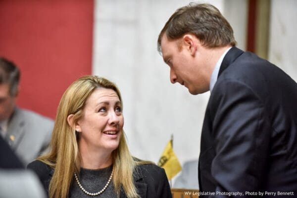 A female lawmaker speaking to a standing man.