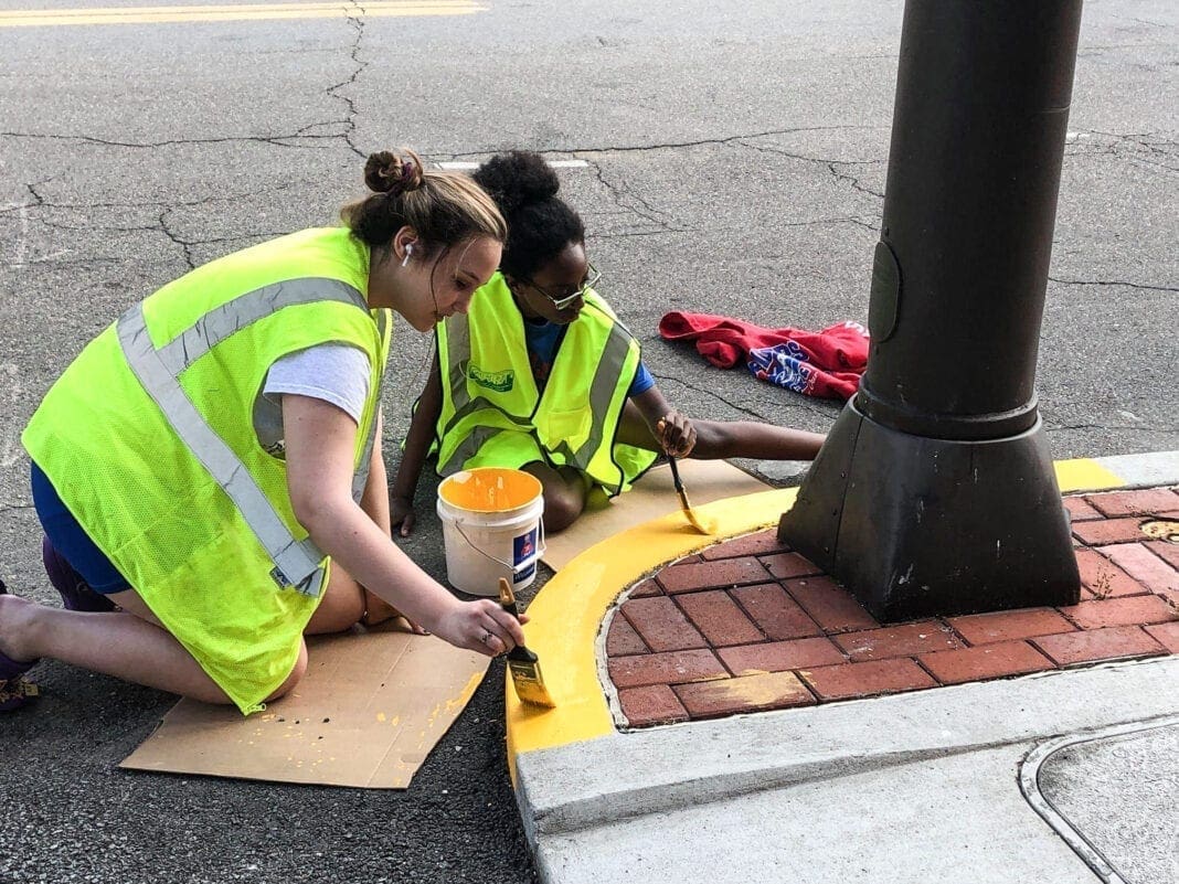 Two young ladies painting a curb.