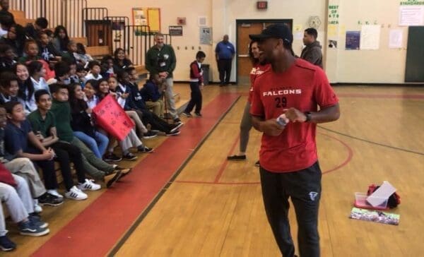 A black man speaking with a group of kids.