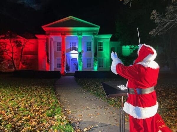 A Santa conducting music in front of a mansion.