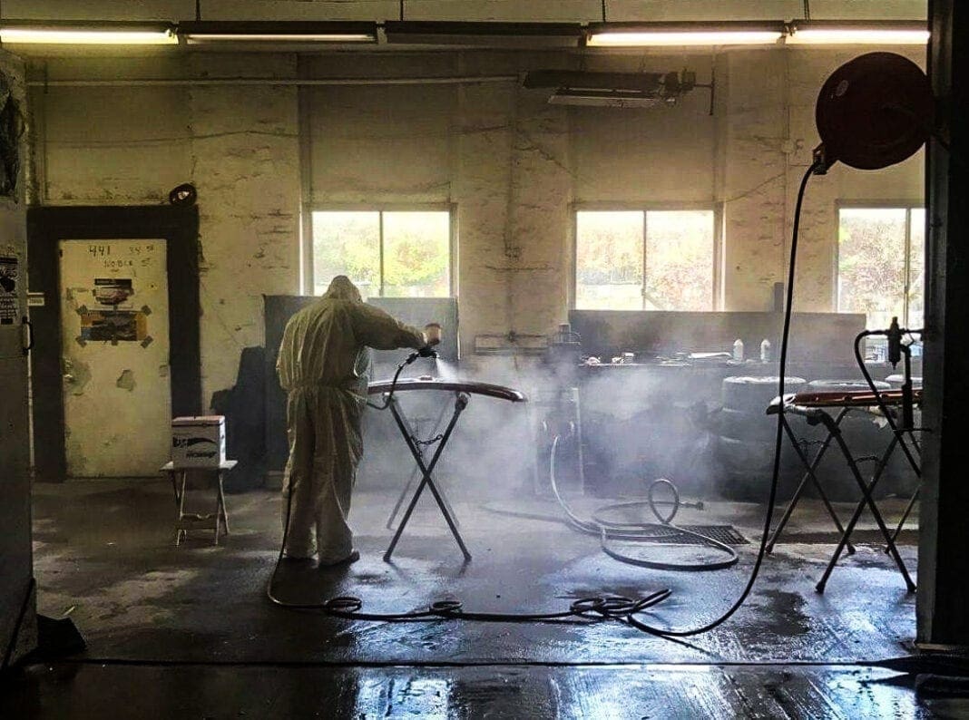 A man airbrushing a fender in a shop.