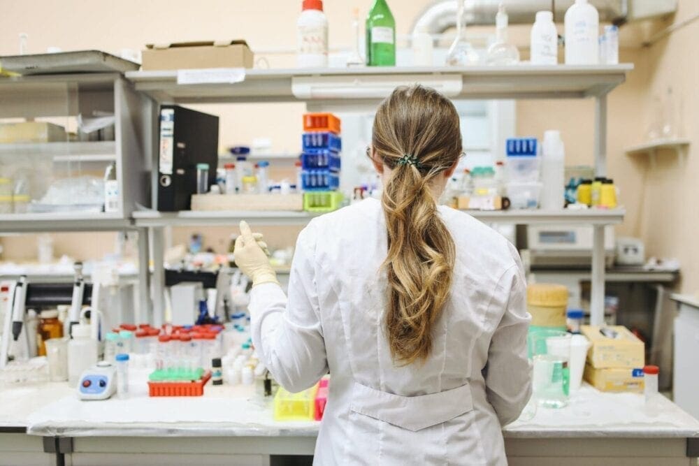 woman in white long sleeved laboratory gown standing. Pharmacy Image