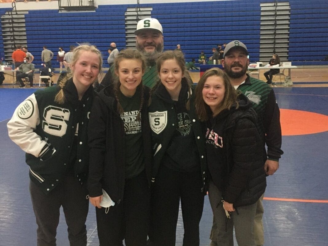 Four girls' wrestlers stand with their coaches after the district wrestling tournament.