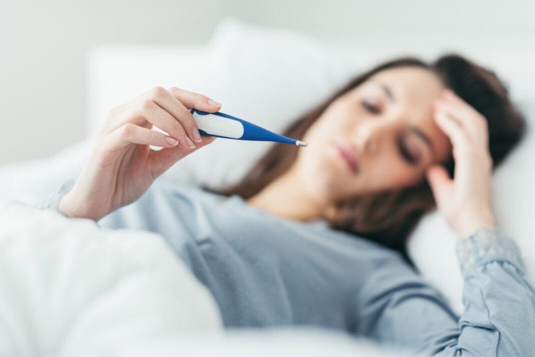 A female looking in a thermometer while in bed.