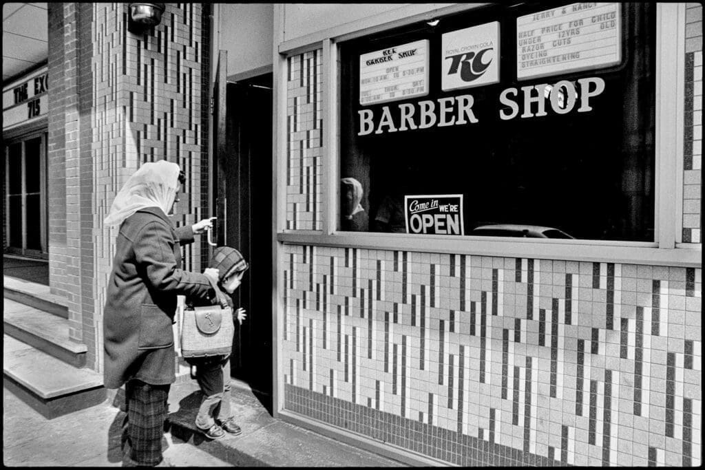 A mother and child going into a barber shop.