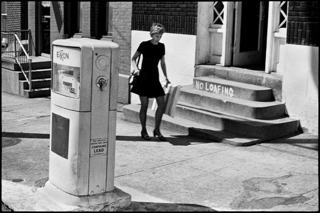 A woman walking past a gas pump.