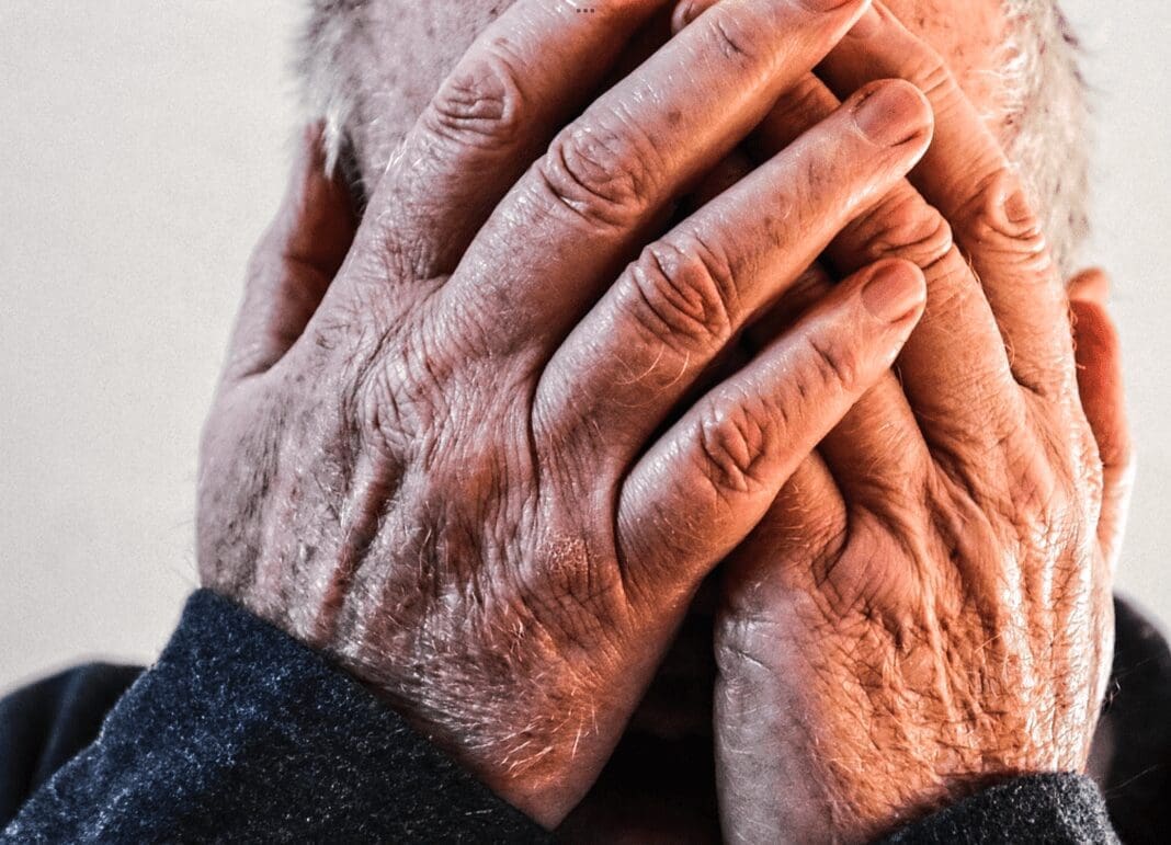 An older person with the hands on their face.